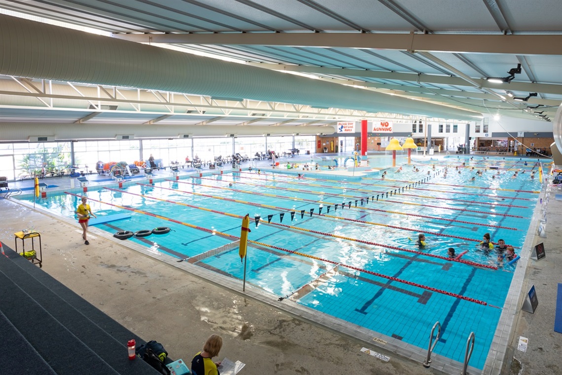 A view from inside the Noarlunga Aquatic Centre showing a large pool containing pockets of swimmers and a lifeguard patrolling on one side.