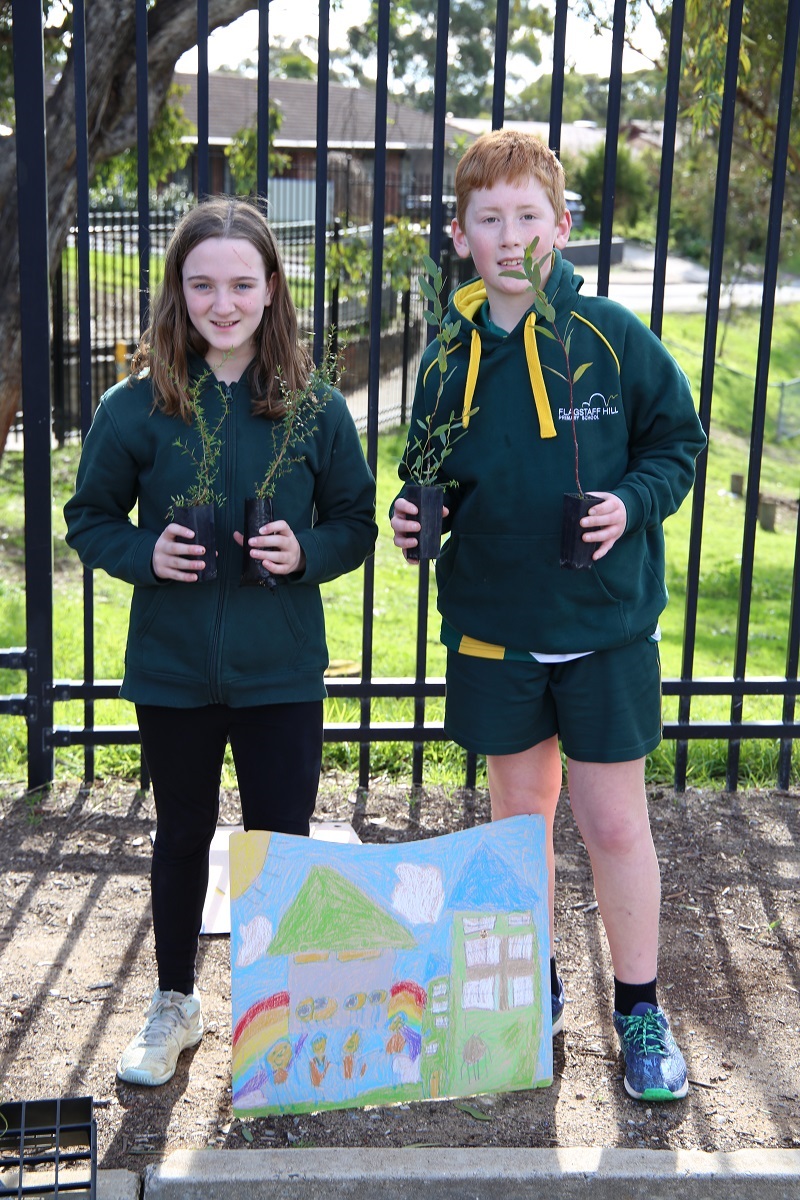 Two students hold trees ready for planting and smile at the camera.