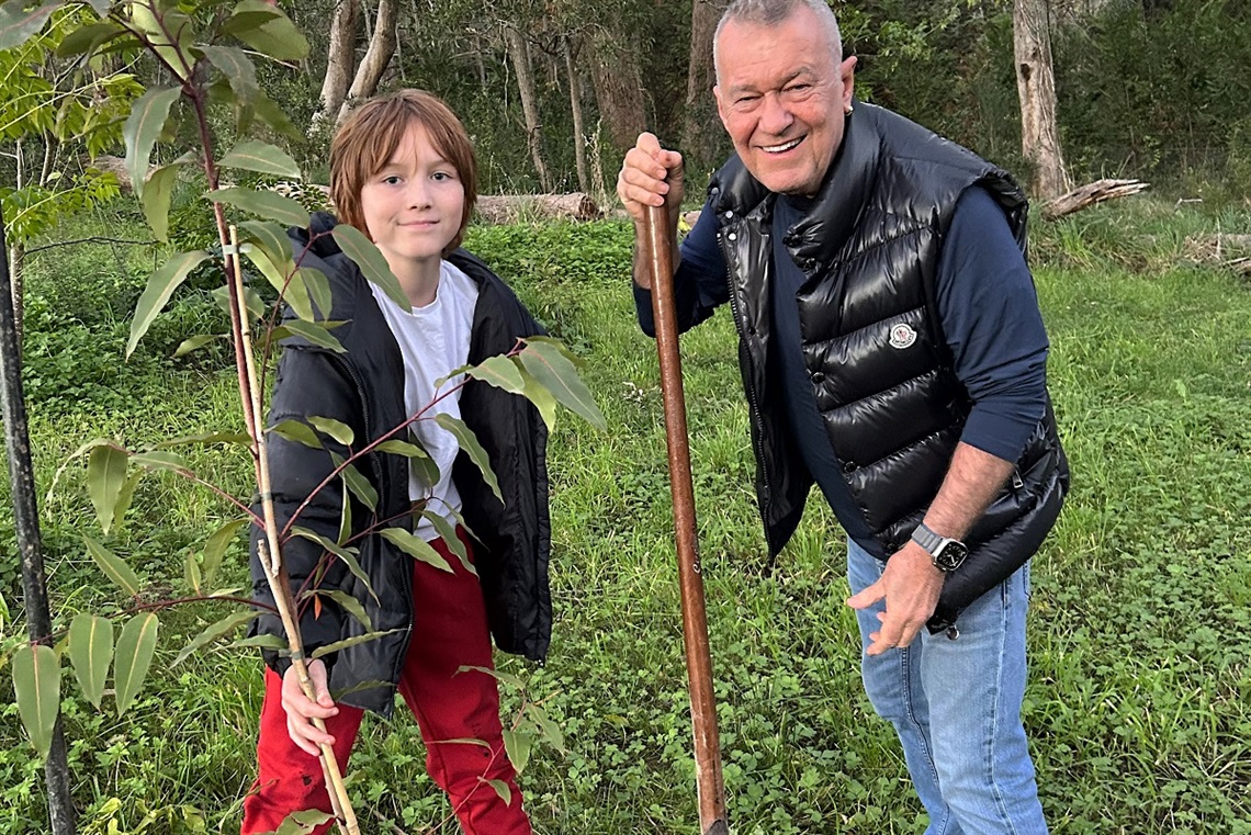 Australian rock legend Jimmy Barnes smiles alongside grandson Dylan as they plant a tree on a property.