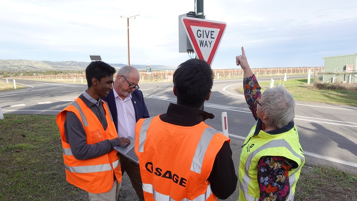 Leon Bignell MP, Onkaparinga Mayor Moira Were and employees of SAGE Automation inspect the new RJAWS signage in McLaren Vale while wearing high-vis vests.