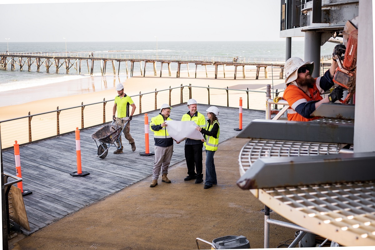 RMK Building Group’s Tom, Robbie and Marianne plan their day’s work on a timber decking by the beach in Port Noarlunga.