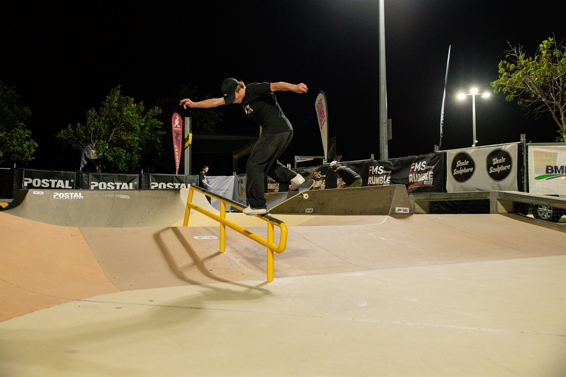 A skateboarder in black clothes grinds along a rail at a skate park at night.