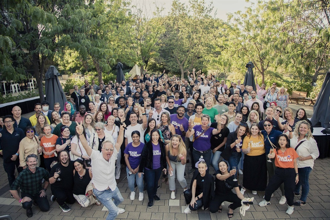 A large crowd of smiling festival participants cheer for the camera, which looks down at them.