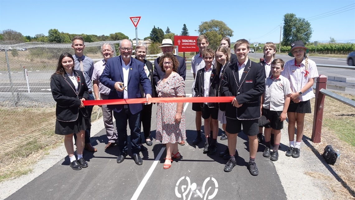 A group of students and Tatachilla Lutheran College staff stand alongside Leon Bignell MP and Onkaparinga Councillor Marisa Bell. A red ribbon is in front of them as they prepare to officially open a new shared-use path, which they're standing on.