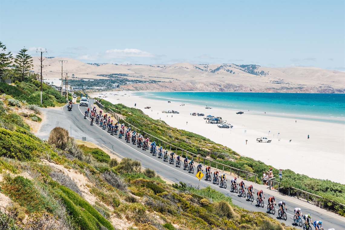 A long line of Tour Down Under cyclists race along Onkaparinga's coastline on a sunny day.