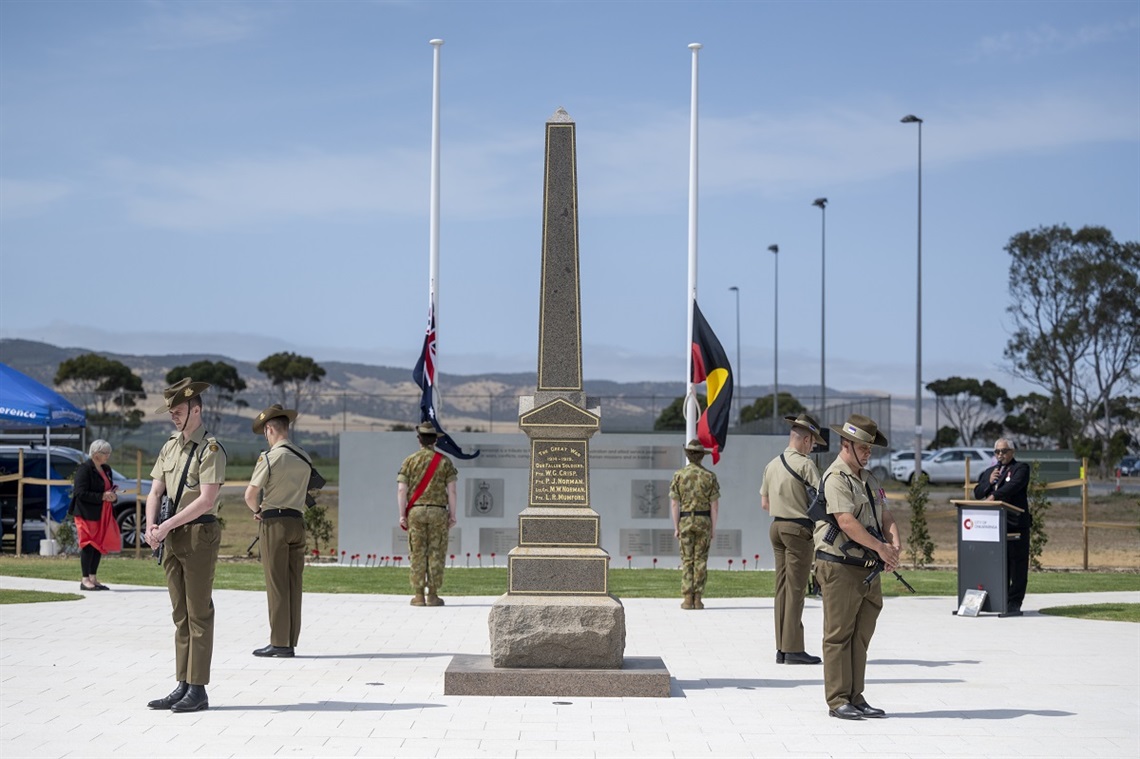 A group of defence force personnel in uniform stand solemnly alongside the Aldinga War Monument at the opening of the new Aldinga War Memorial. 