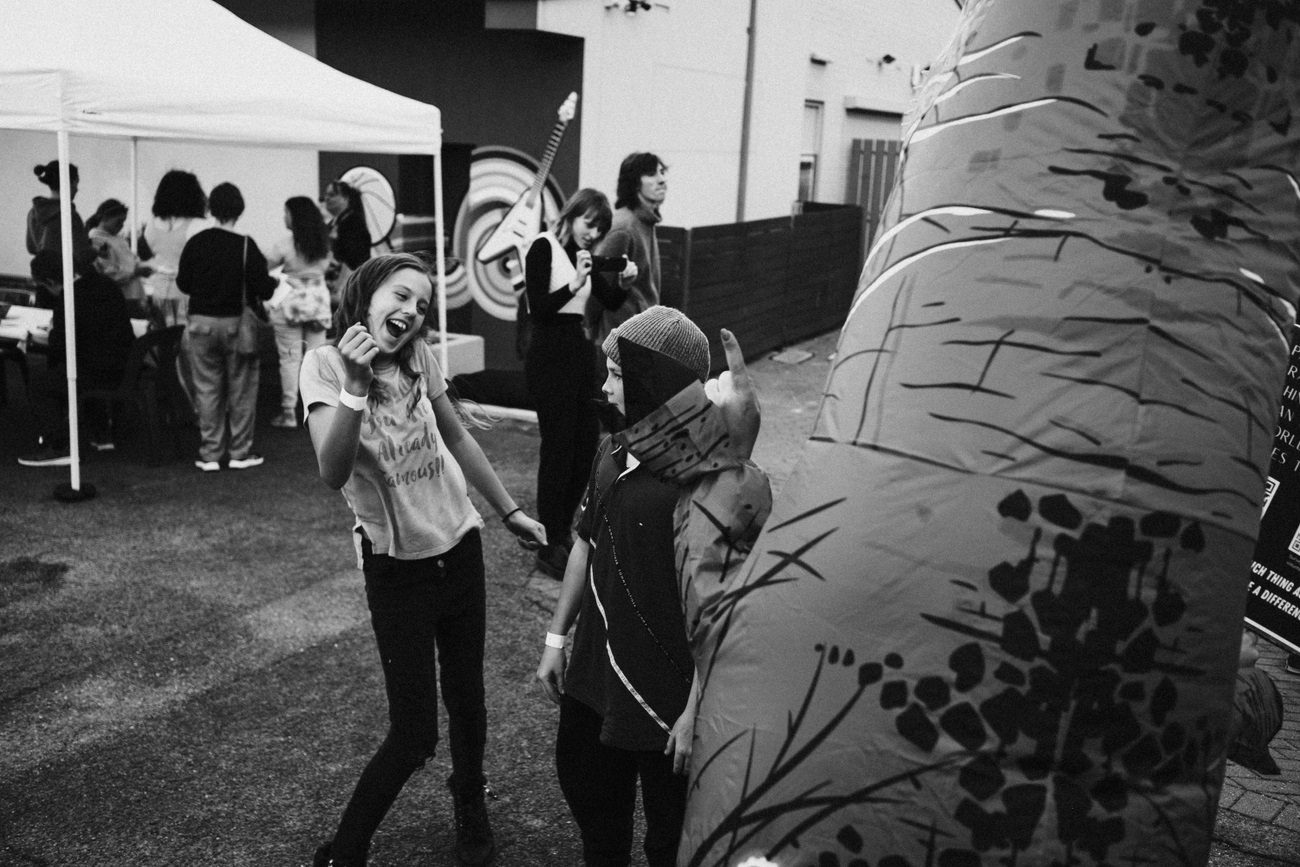 A pair of young people talk and laugh in black and white with more people milling in the background.