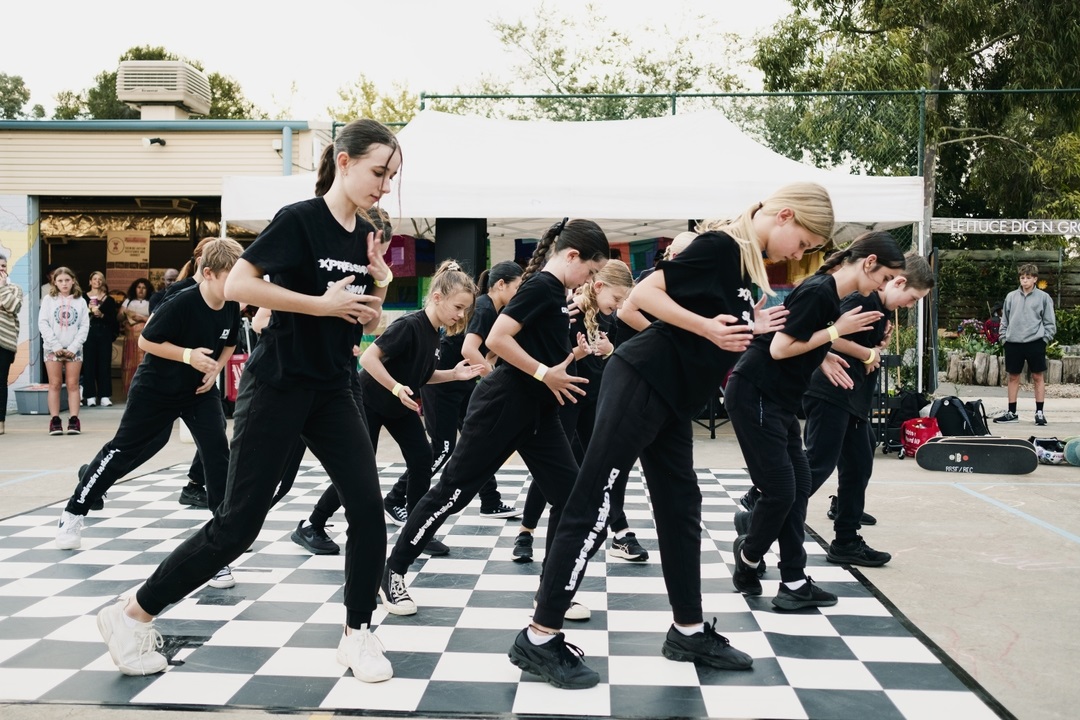 A group of dancers wearing black clothes dances on a black-and-white checked mat.