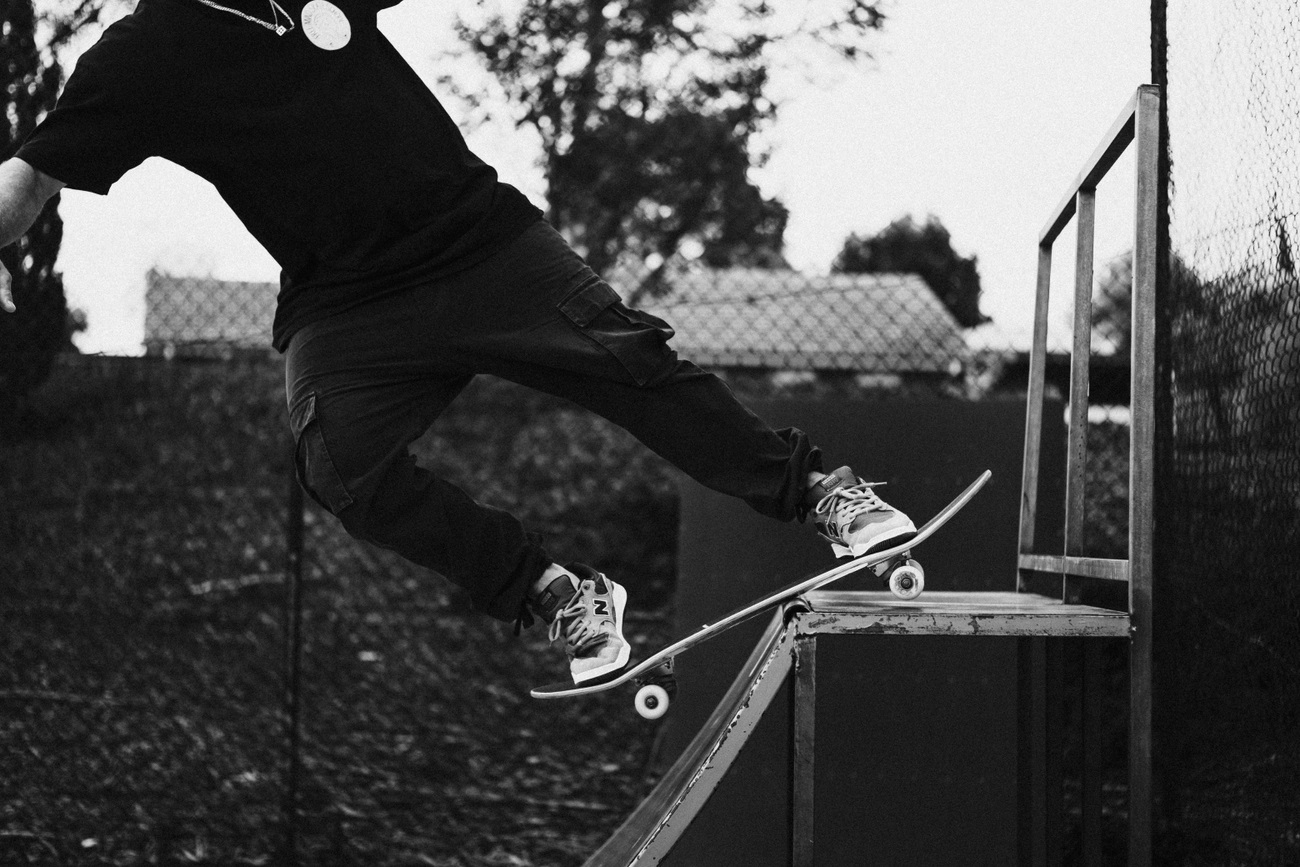 A black-and-white photograph of a skateboarder suspended on his board over the coping of a half-pipe.