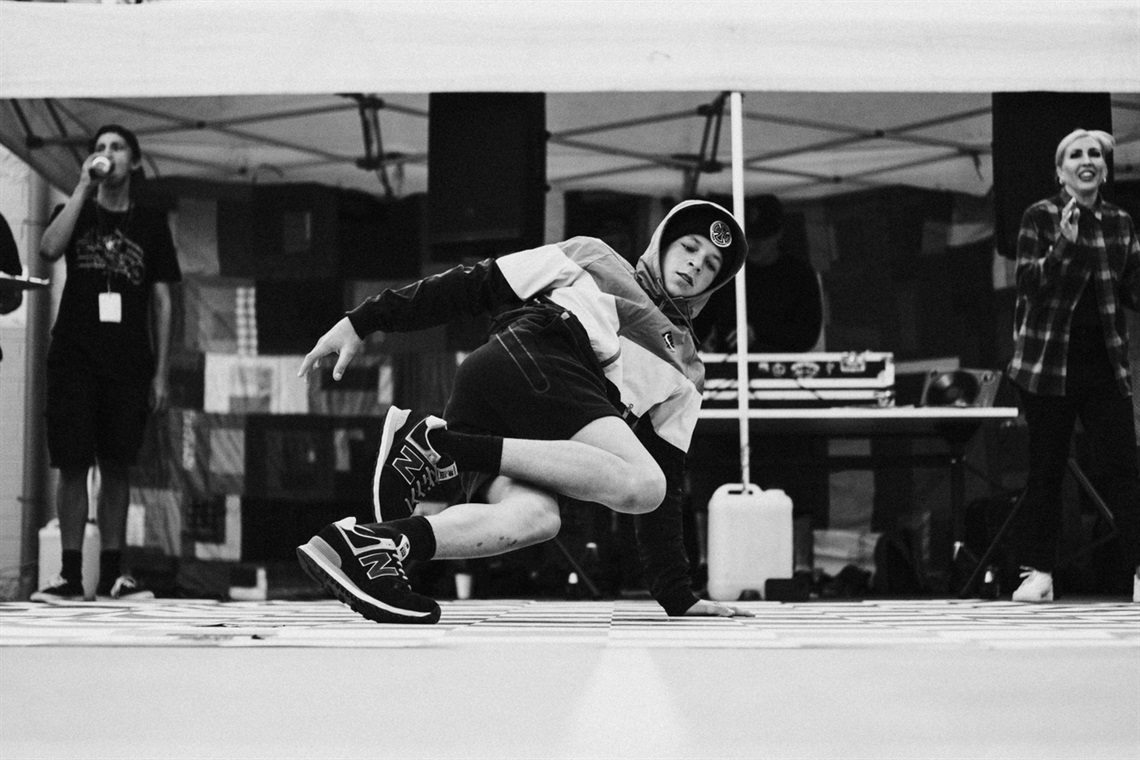 A young performer photographed in black-and-white breakdances on stage.