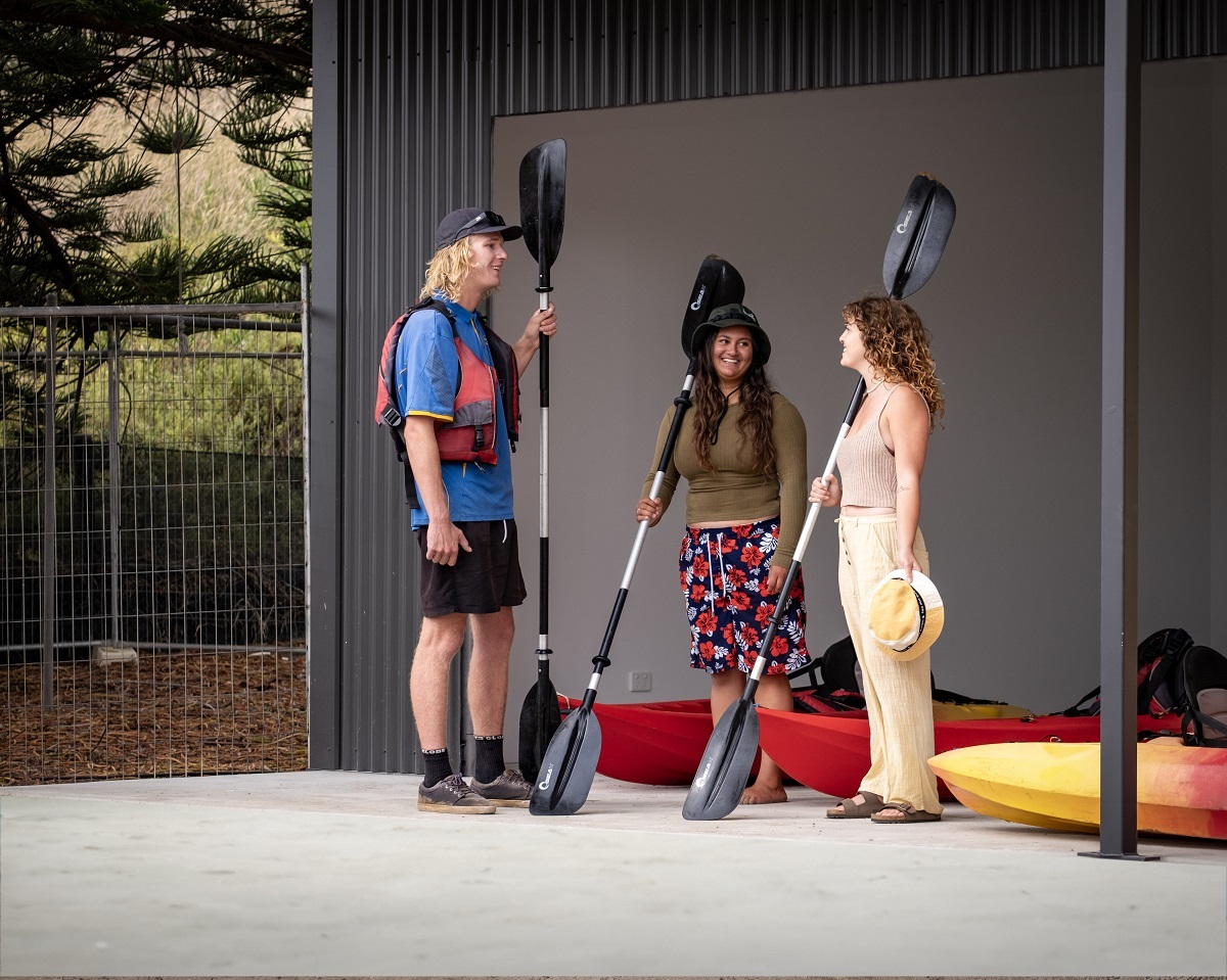 Three kayakers smile inside the new facility at Wearing Street with kayak paddles and kayaks alongside them.