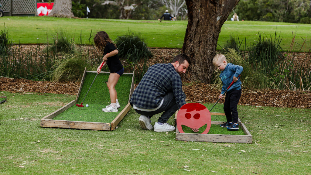 A father plays mini golf with his two young children.