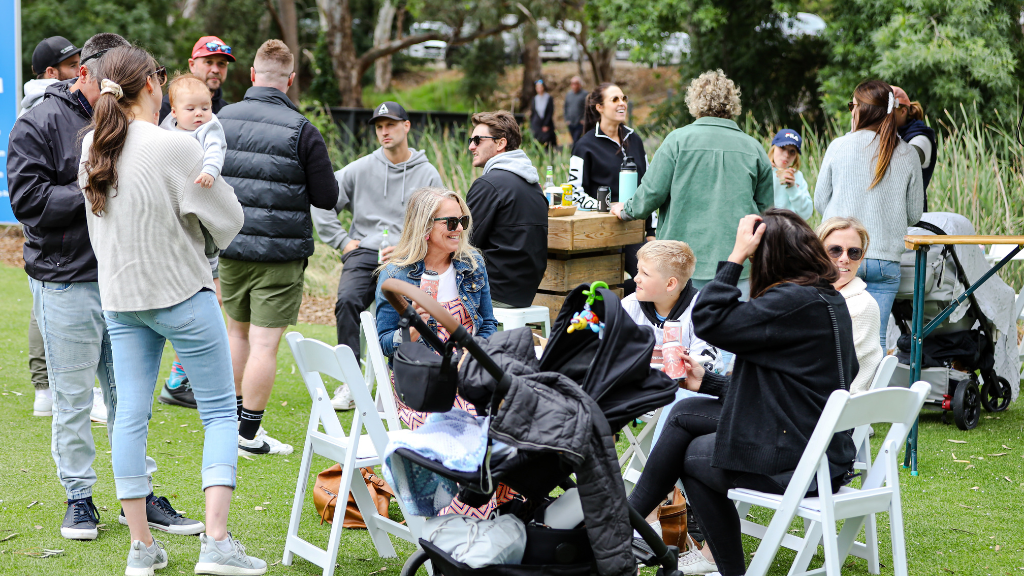 A crowd of people sit and stand while chatting on grass at the 2023 Webex golf contest in Willunga.