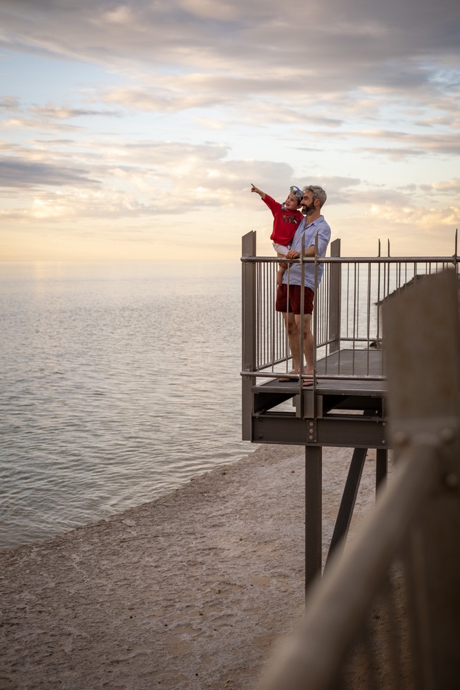 A man holds his young son on the Witton Bluff Base Trail boardwalk as the boy points out to the sea.