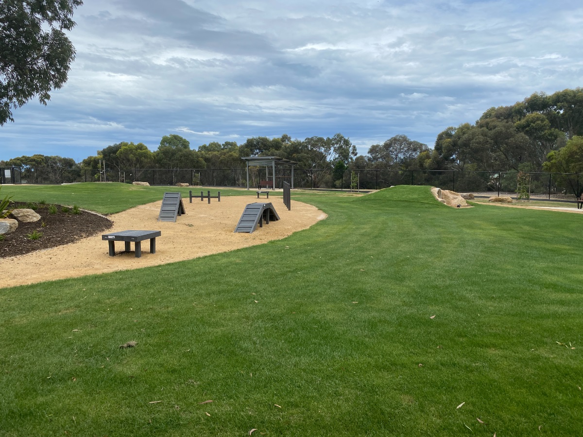 The grassy are of Woodcroft Dog Park with agility equipment 