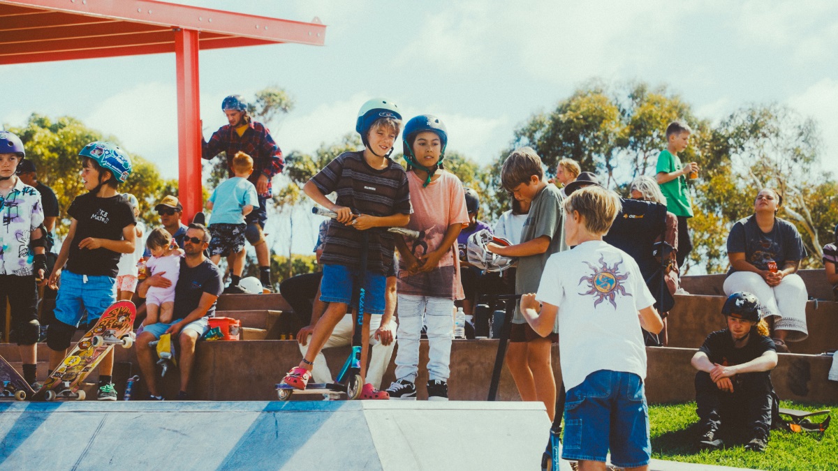 A crowd of skateboarders and scooter riders smile and talk at the Aldinga skate park.