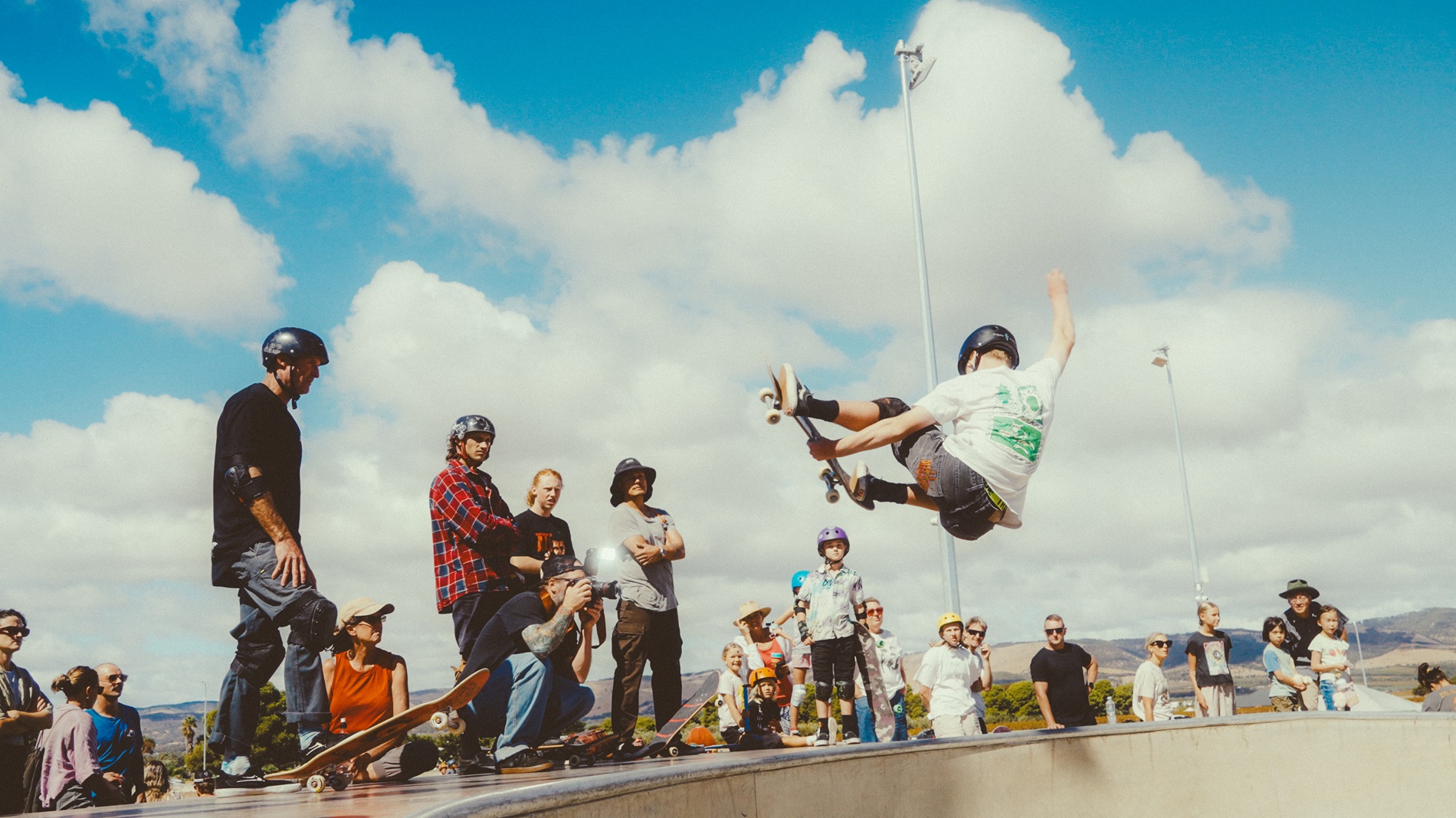 A skateboarder grabs his rail as he flies through the air out of the Aldinga skate park bowl as onlookers watch his air.