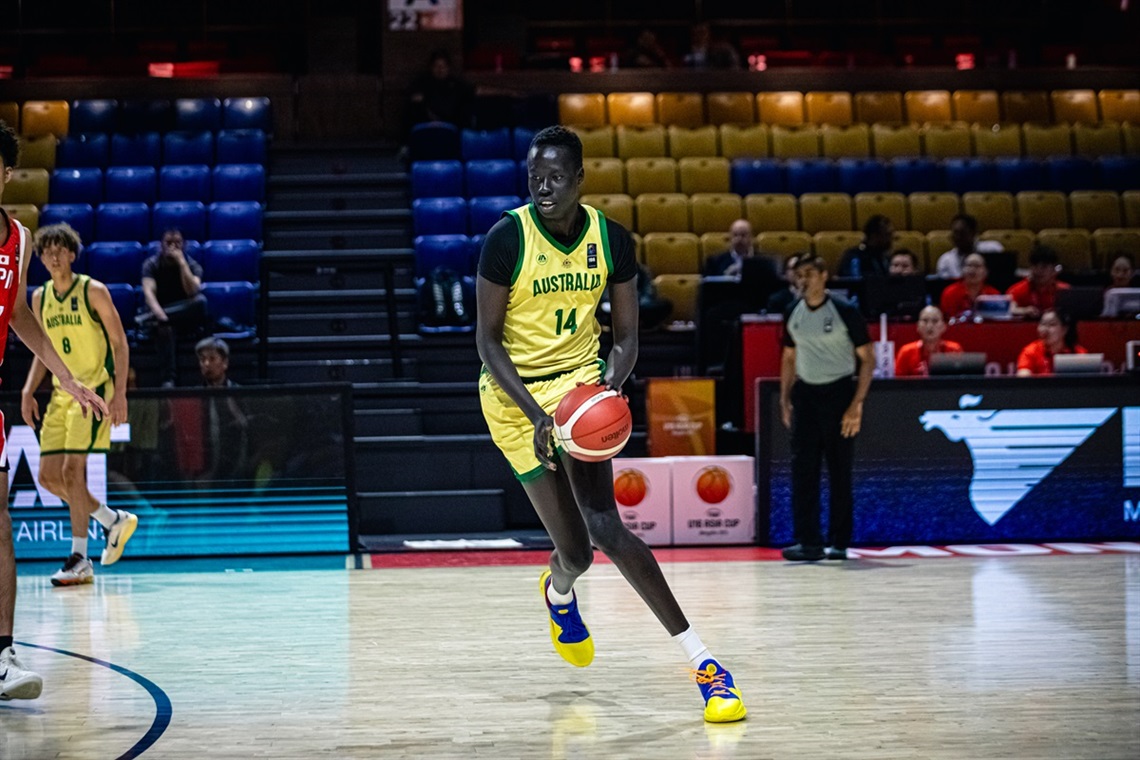 Basketballer Awak Machar dribbles the ball with concentration on a court wearing his green and gold Australia uniform.