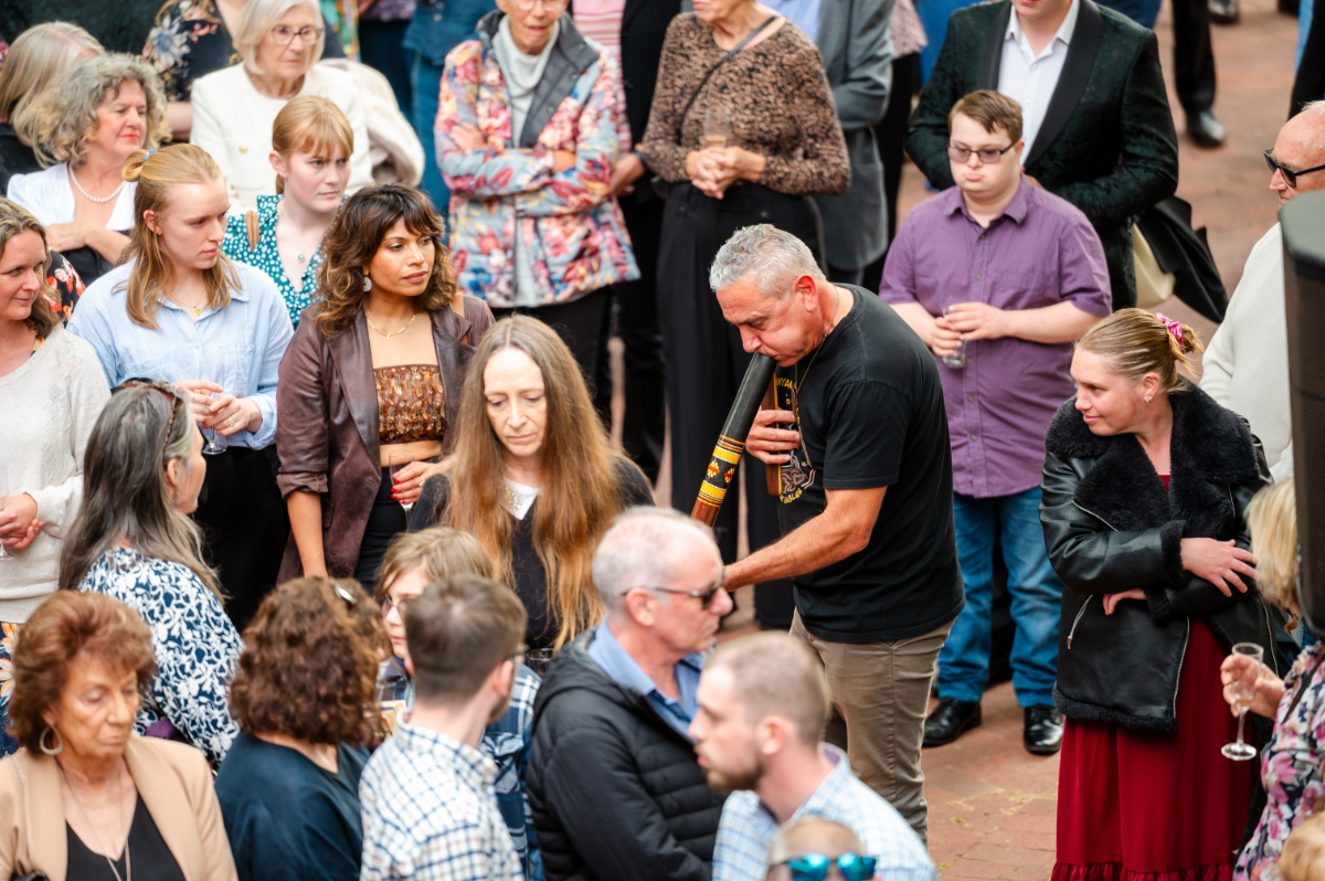 A crowd of people watch Karl Telfer play a didgeridoo.