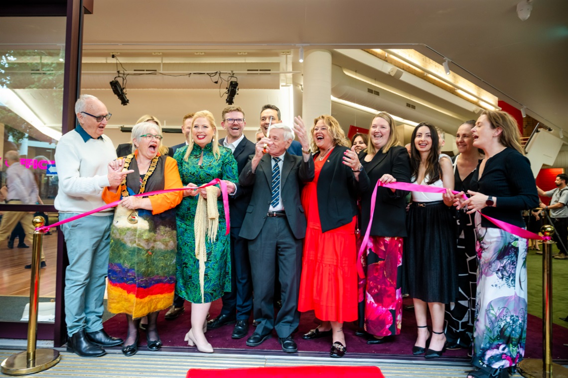 A crowd of dignitaries smile and laugh after cutting the ribbon to officially open the upgraded Hopgood Theatre.