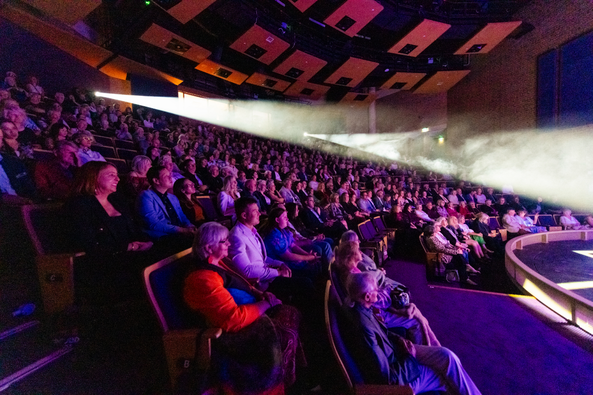 A view from alongside the rows of seating at the Hopgood Theatre with the spotlights trained on the stage amid the dark.