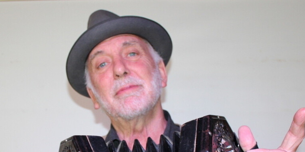 A man in a bowler hat plays a black accordian.