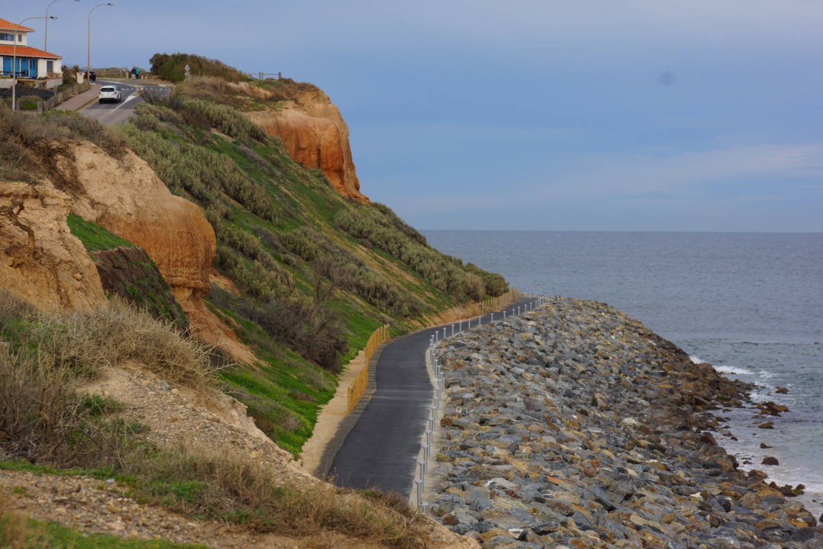 A view looking towards Witton Bluff with an asphalt path extending around the cliffs, with upgraded seawall rocks to the north.
