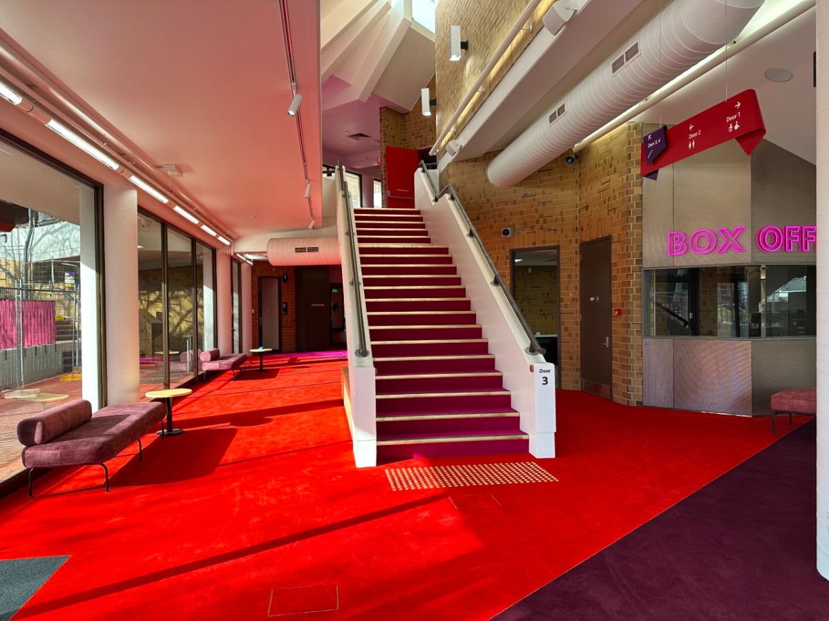 A view from the recently upgraded Hopgood Theatre interior, its red carpet, stairway and box office with bright pink signage.