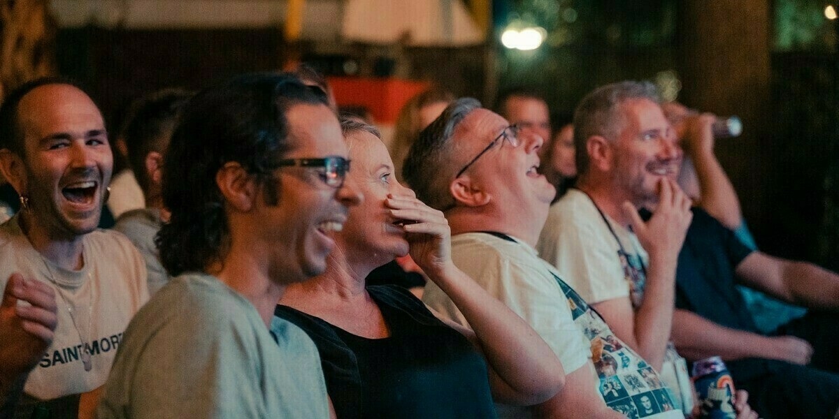 A group of audience members at a comedy show laugh in their seats.