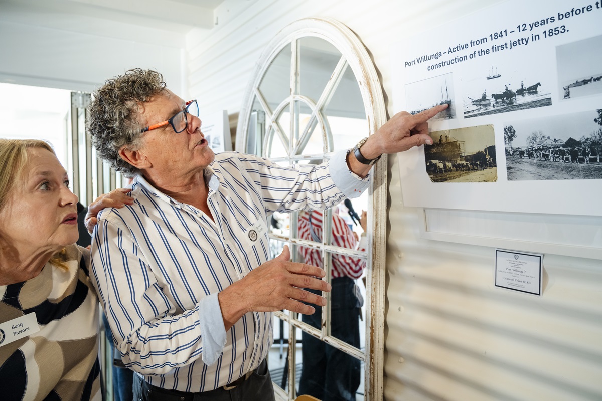A pair of people discuss historical photos as the man points to a display board at the Port Willunga 175th anniversary event.