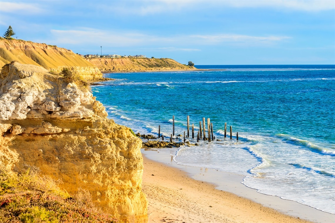 A clifftop view of Port Willunga beach and the timber remains of the Port Willunga jetty jutting out of the water.