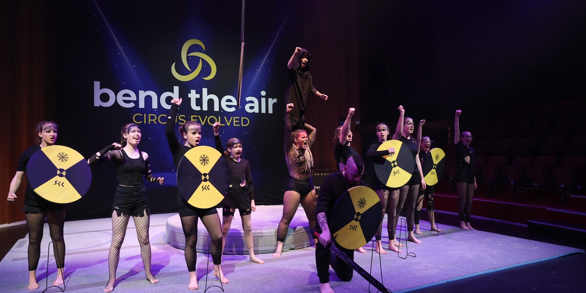 A group of circus performers shout on stage with their fists raised in the air.