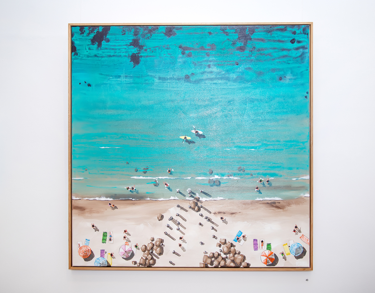 A photo of a painting hung at the arts centre depicting an idyllic beach scene from above.