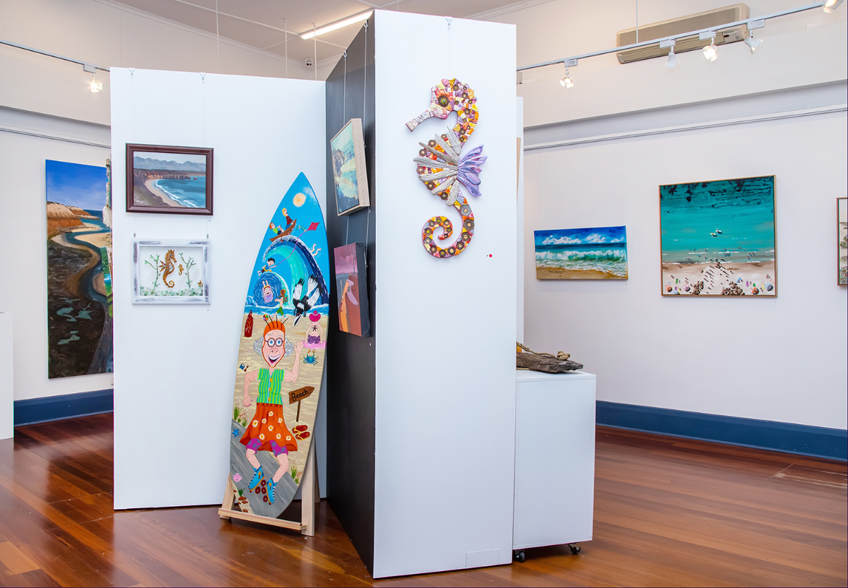 A pulled-back shot of the arts centre gallery with various surf-inspired works hanging on the walls.