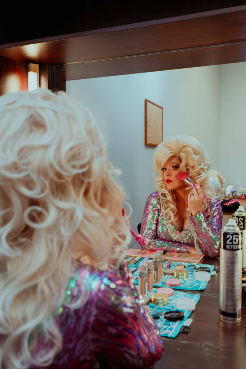 Dolly Parton tribute performer Brooke McMullen applying makeup in a backstage mirror.