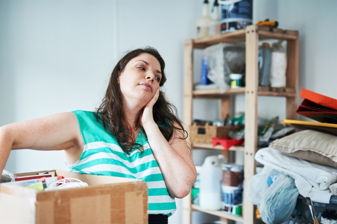 A woman looks exasperated in her shed with the amount of items she needs to clean up.