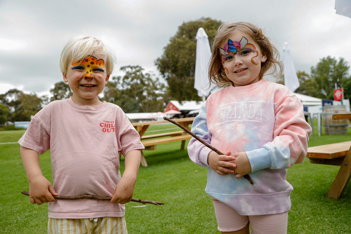 Two young children with face paint smile at the camera in colourful pink clothing.