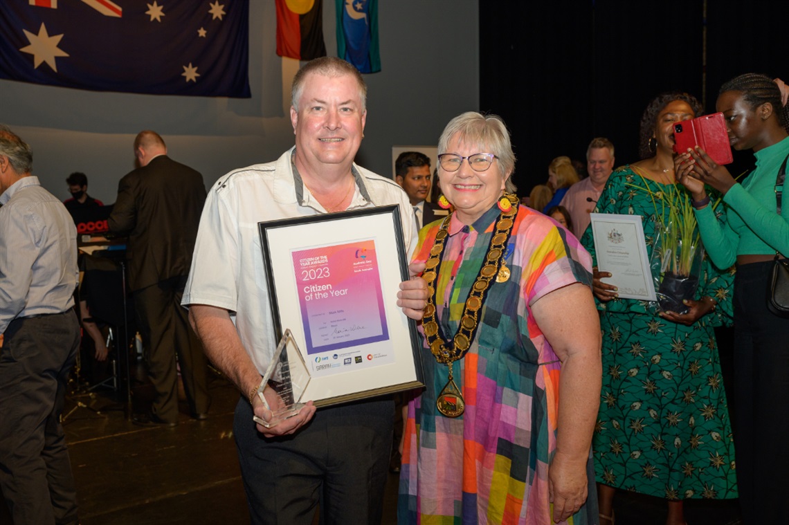 Citizen of the Year Award recipient Mark Mills holds his award and smiles alongside Onkaparinga Mayor Moira Were.