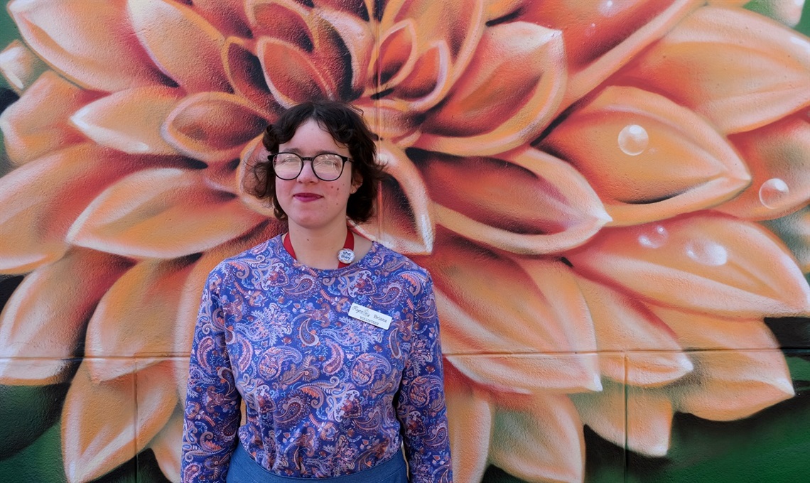 Volunteer Briana Taylor stands in front of a colouful flower mural at Reynella Neighbourhood Centre.