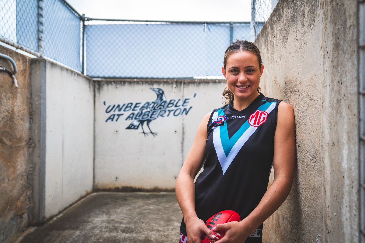Port Power AFL player, Indy Tahau, smiles at the camera with a football in her match day uniform.