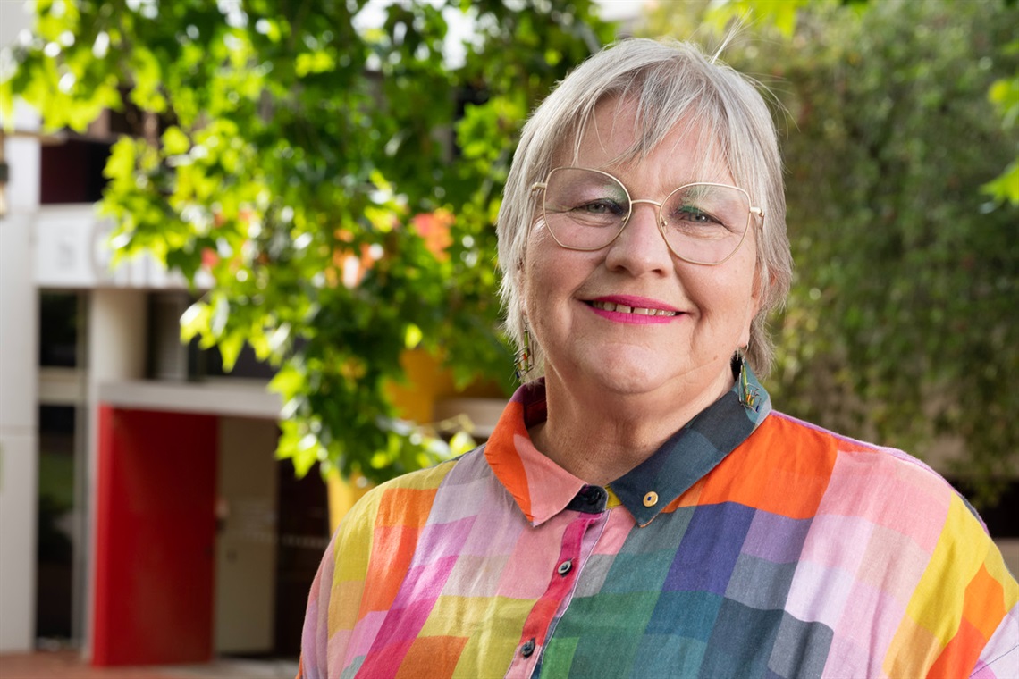 Mayor Moira Were in a multi-coloured dress smiles in front of a leafy green tree at Noarlunga's council offices.