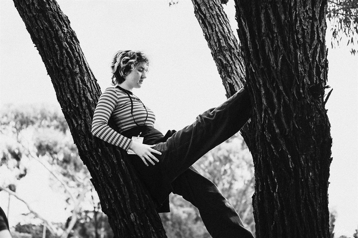 A black-and-white photograph of young event organiser, Pearl George, standing on a tree trunk.