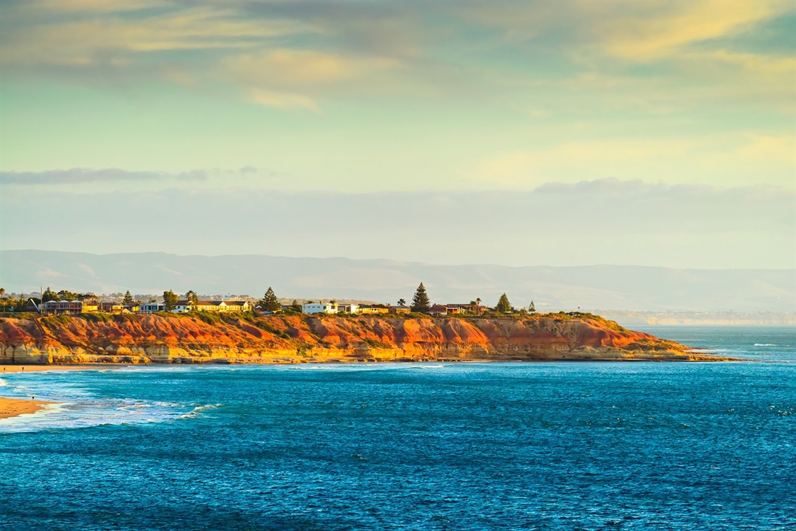 A view of the golden cliffs and blue ocean of South Port beach, taken from the Port Noarlunga jetty in late afternoon sun.