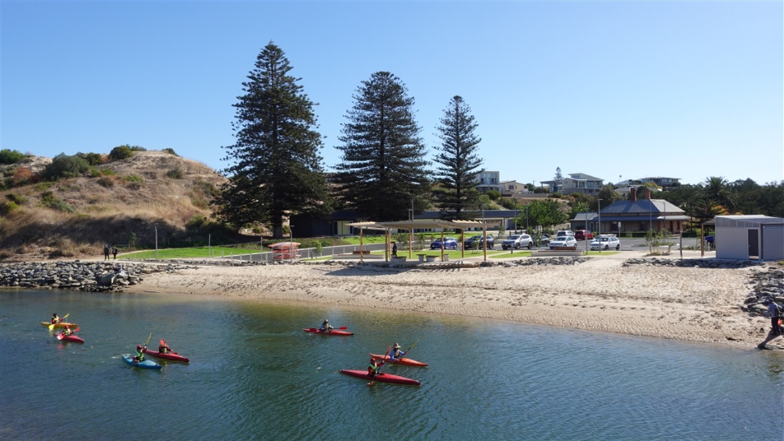 Kayakers paddle down the Onkaparinga River past the sandy riverbank of the newly redeveloped Wearing Street precint.