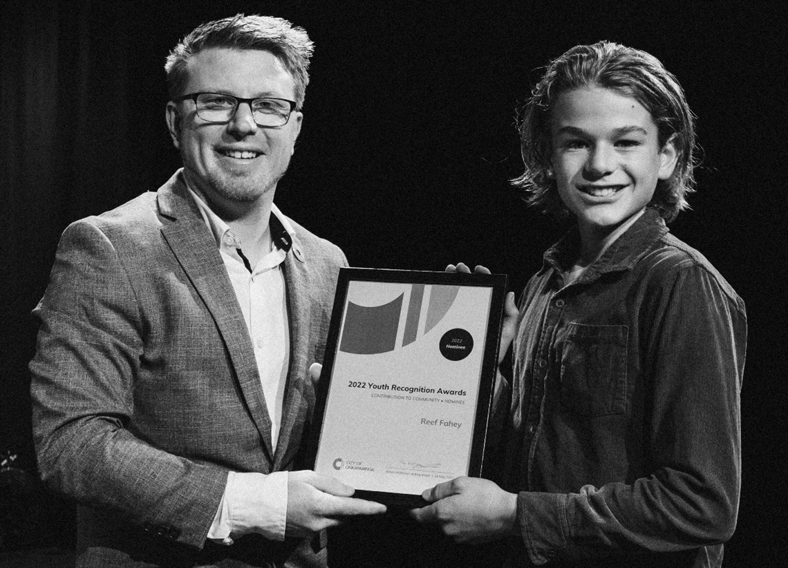 A black and white photograph of acting mayor Simon McMahon presenting an award to Contribution to Community Award recipient Reef Fahey.