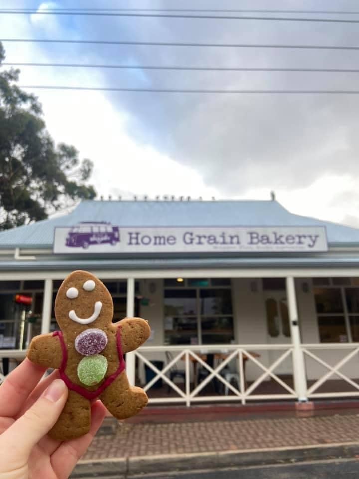 A hand holds up a gingerbread man in front of the Home Grain bakery entrance.